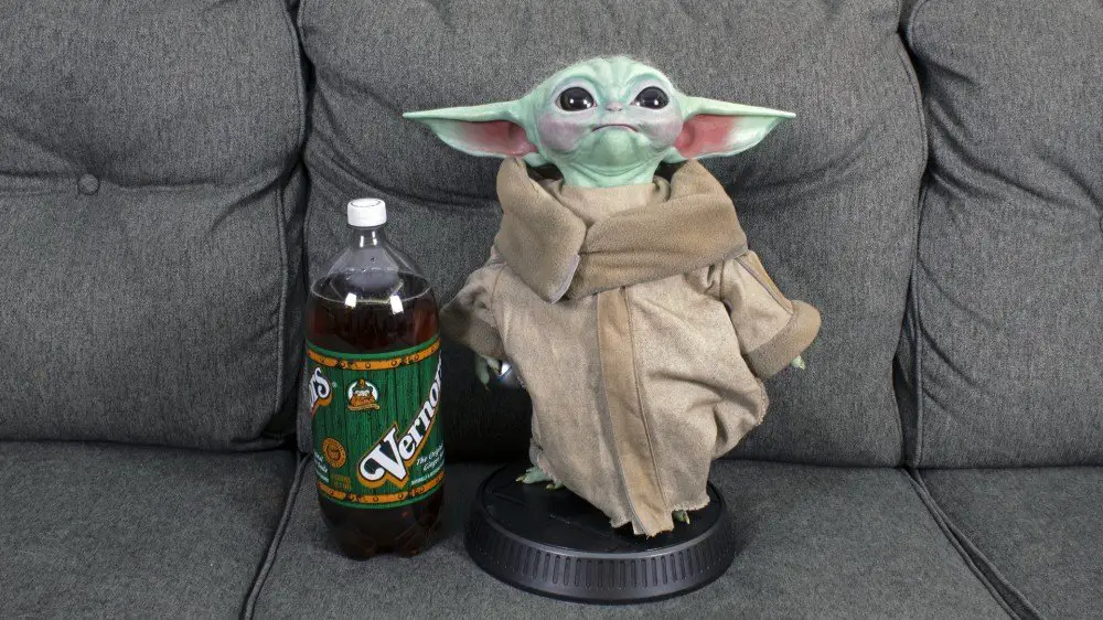 Baby Yoda de pie más alto que una botella de refresco de 2 litros.