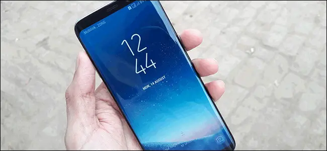 Una mano que sostiene un Samsung Galaxy S8 con la pantalla táctil que muestra la hora y la fecha.