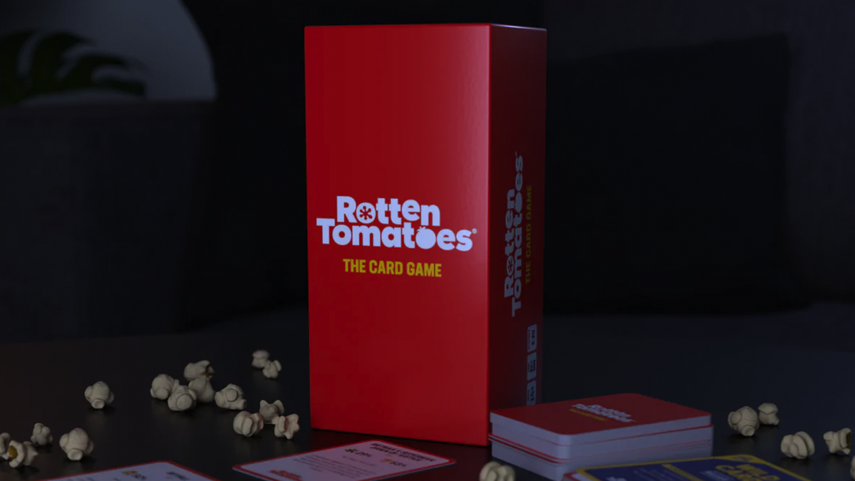 El paquete del juego de cartas Rotten Tomatoes en una mesa rodeada de palomitas de maíz.