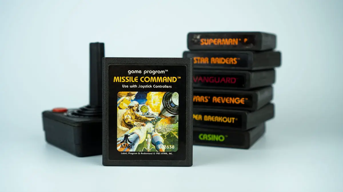 Cartucho de videojuego Missile Command junto a un controlador Atari clásico y una pila de otros juegos.